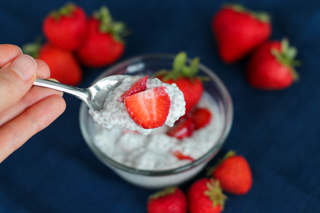 Hand holding up spoon filled with strawberry cheesecake chia seed pudding