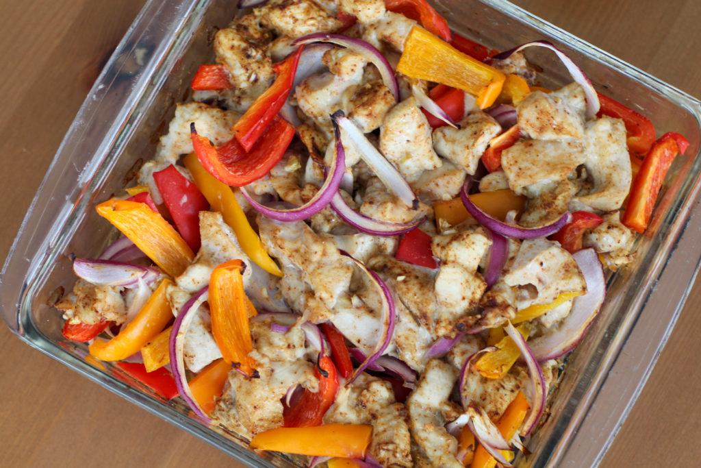 Glass dish of baked chicken fajitas at an angle