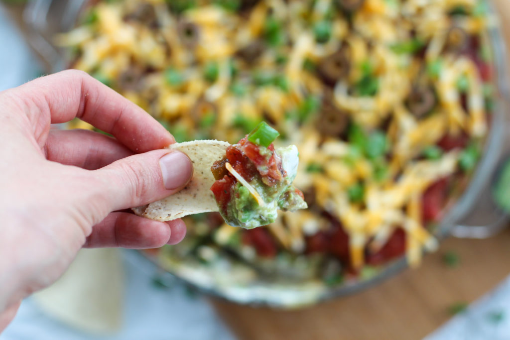 hand holding chip with keto 7 layer taco dip