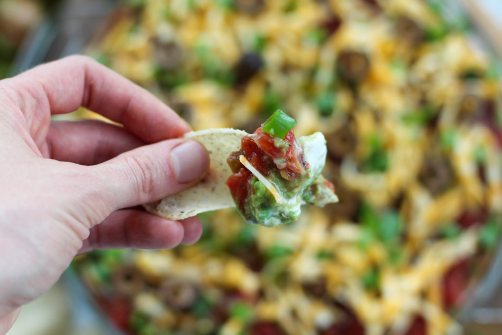 hand holding chip with keto 7 layer taco dip