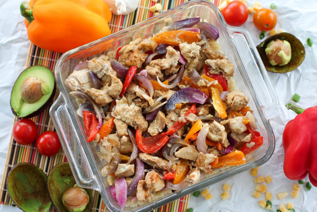 Glass dish of baked chicken fajitas surrounded with veggies