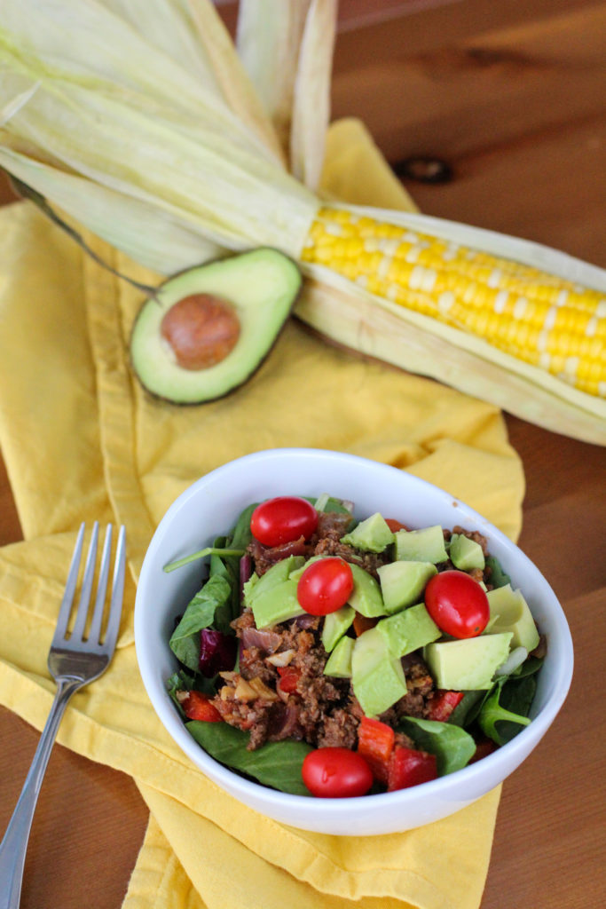 Taco meat salad topped with avocado and grape tomatoes