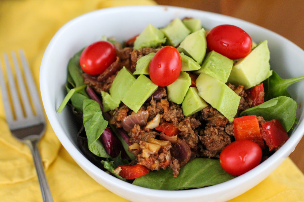 Taco meat on a salad topped with avocado and tomato