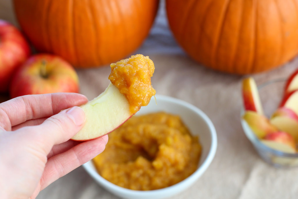 Hand holding apple slice dipped in pumpkin dip