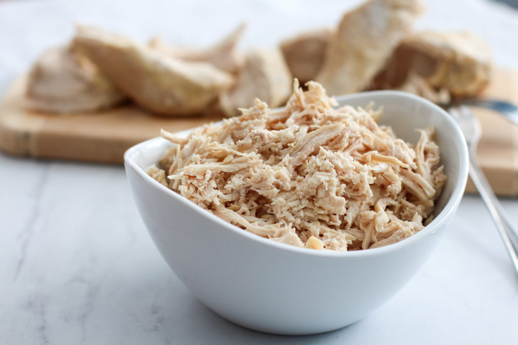 bowl of shredded chicken with cutting board of cooked chicken