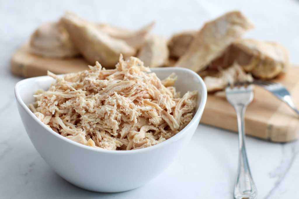 bowl of shredded chicken with cutting board of cooked chicken