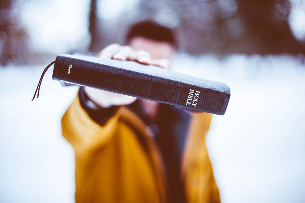 man in yellow coat holding bible out in front
