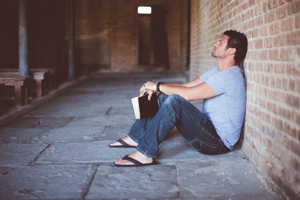 man leaning against brick wall with bible
