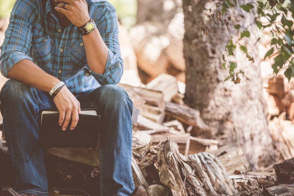 man sitting near wood pile holding bible