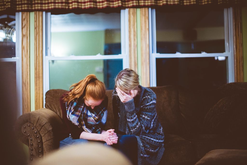 Two women praying together on couch