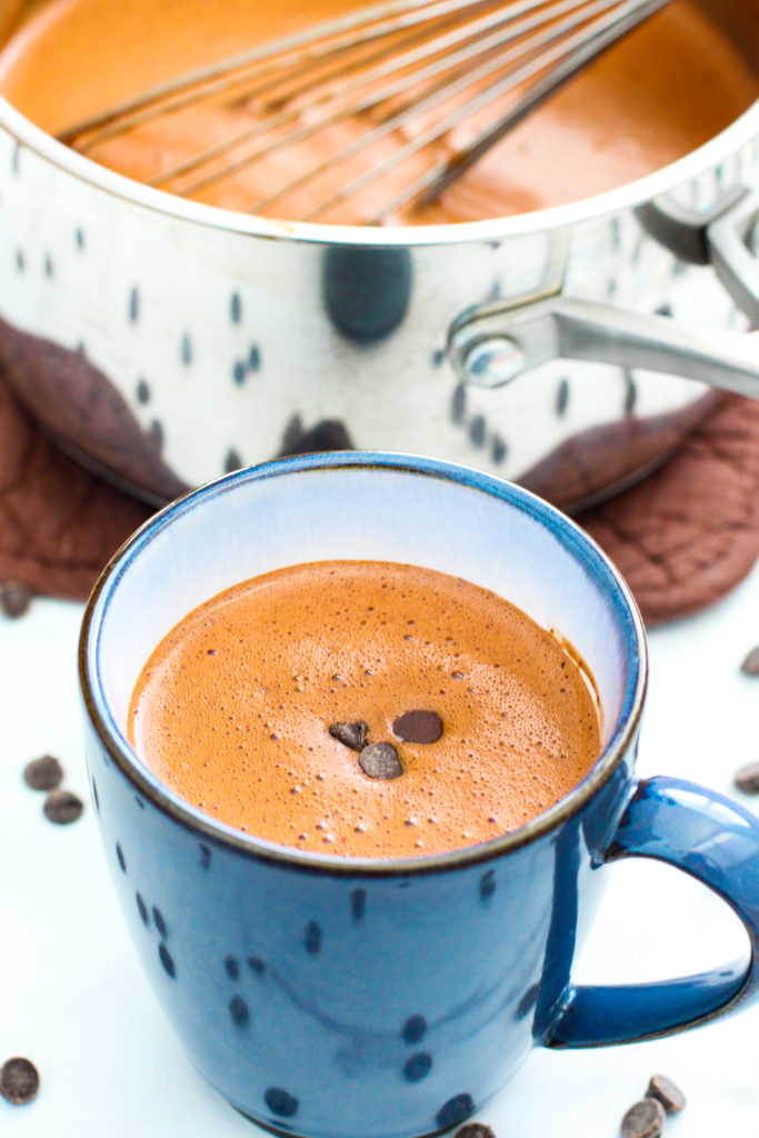 Pan and mug of homemade hot chocolate surrounded with chocolate chips