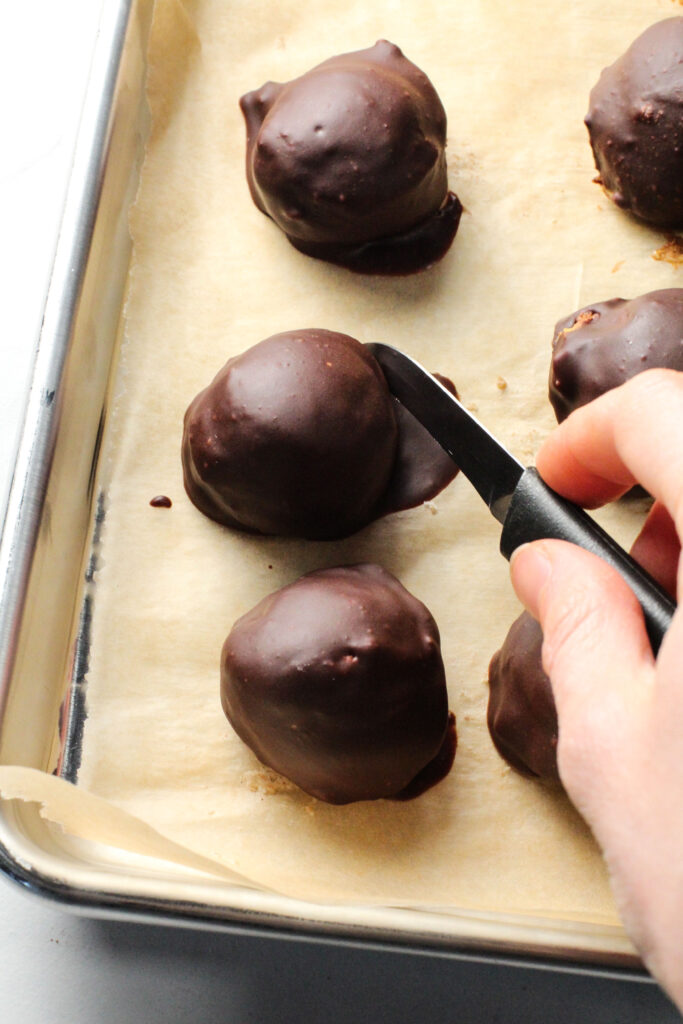 hand holding knife to cut off chocolate edge of truffle