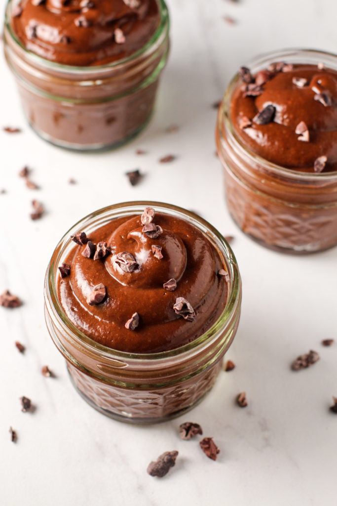 small bowls of chocolate avocado pudding topped with cocoa nibs