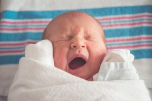 newborn wrapped in blanket yawning