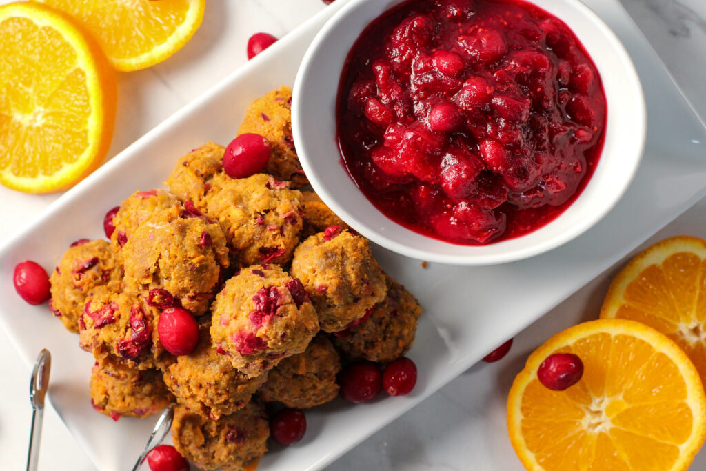 cranberry orange meatballs on white plate with bowl of cranberry sauce