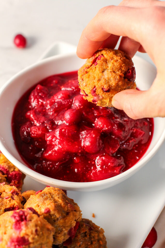 hand about to dip cranberry orange meatball in dipping sauce