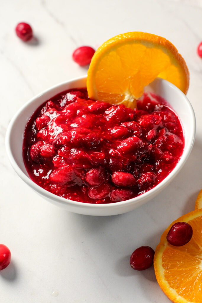 orange cranberry sauce in white bowl with orange slice on side of bowl