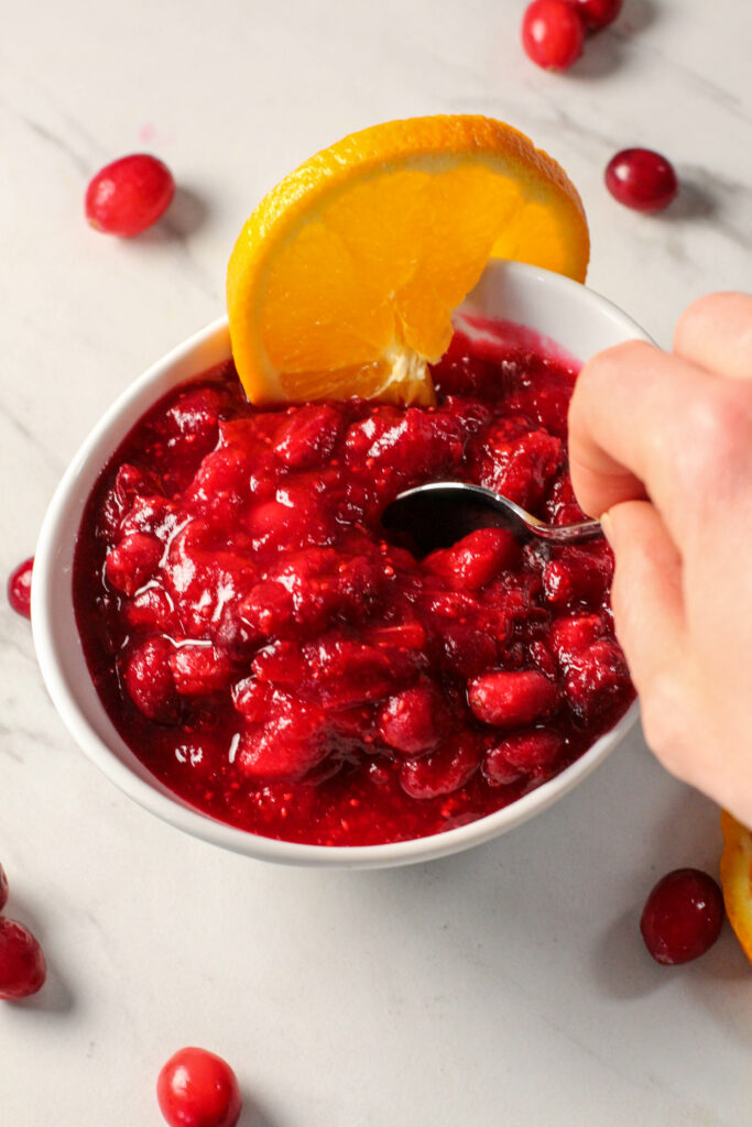 hand holding spoon to get orange cranberry sauce from white bowl