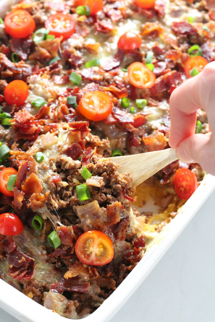 hand holding wooden spoon scooping out bacon cheeseburger casserole