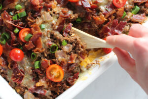 hand holding wooden spoon to scoop out bacon cheeseburger casserole
