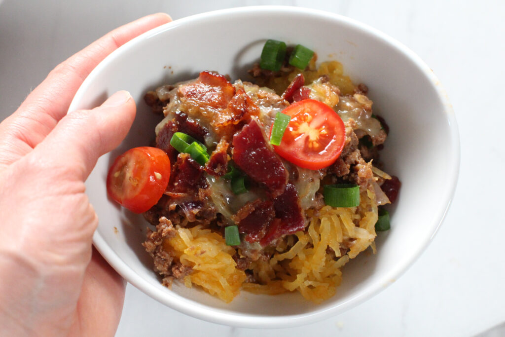hand holding white bowl of bacon cheeseburger casserole
