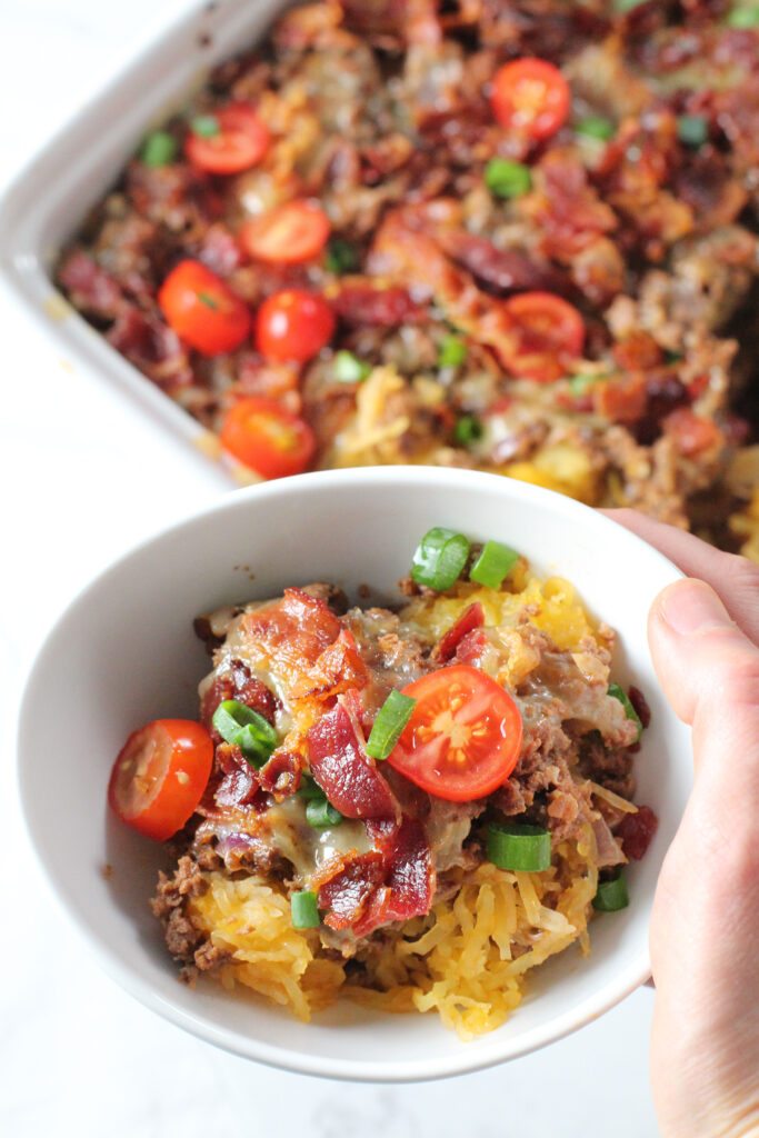 hand holding white bowl of bacon cheeseburger casserole