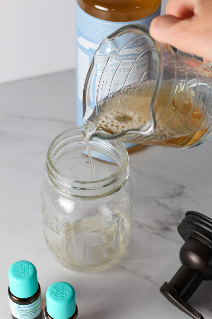 hand holding measuring cup pouring soap into mason jar