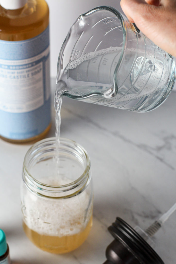 hand pouring measuring cup of water into mason jar