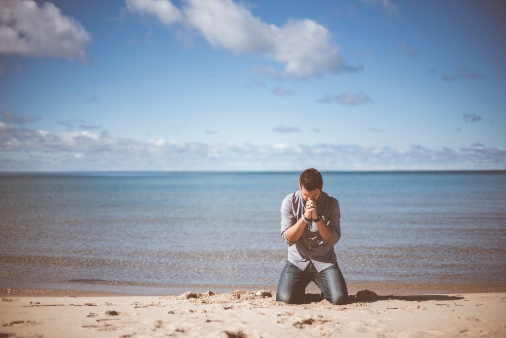 man kneeling in sand praying