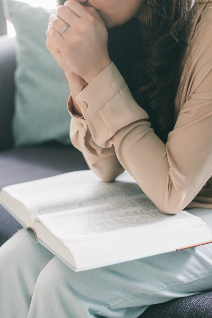 woman with hands folded praying with Bible in lap