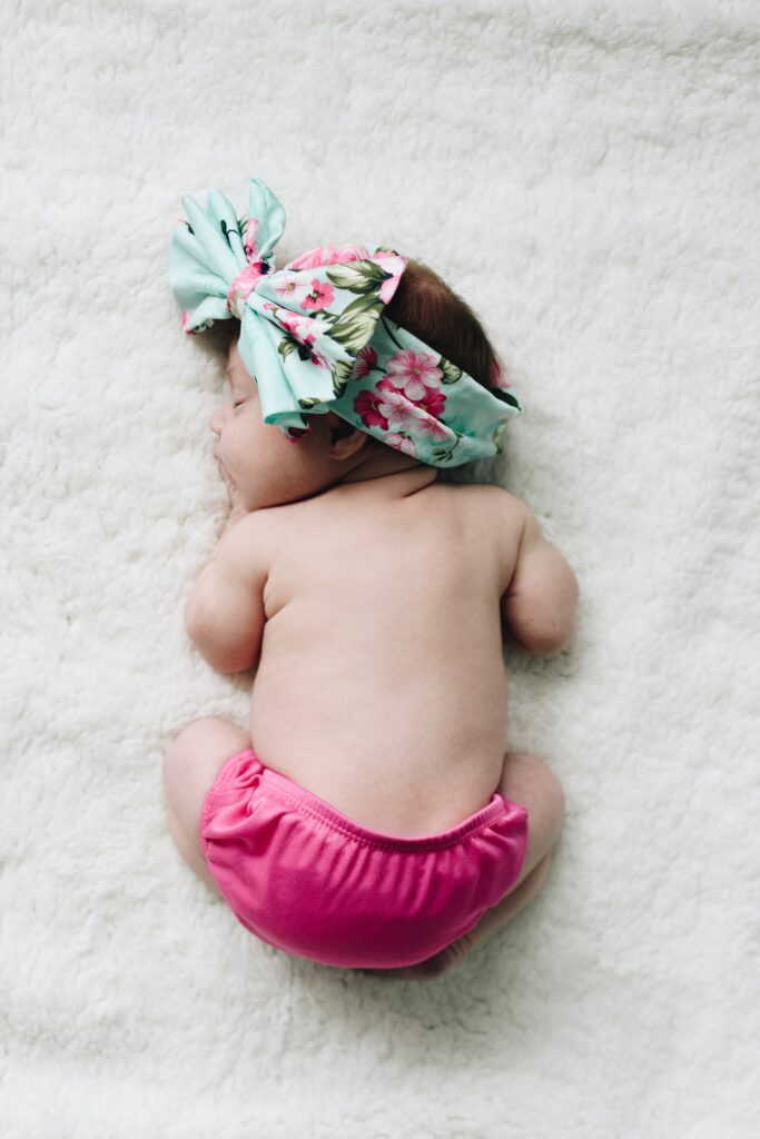 Baby sleeping curled up on the ground with bright pink diaper and large headband