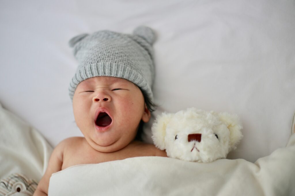 Baby yawning laying next to stuffed animal