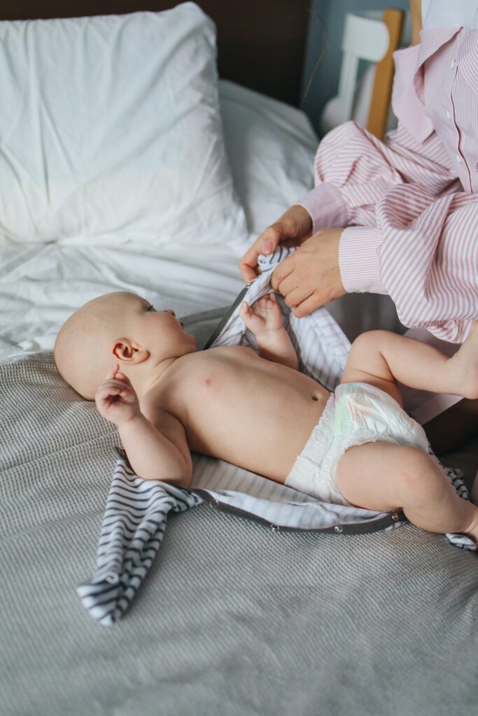 mom dressing baby laying on bed