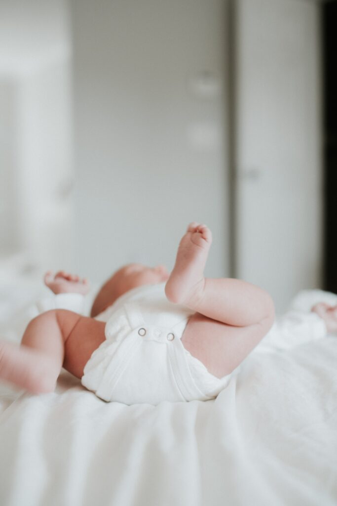 baby in diaper lying on bed with feet in the air