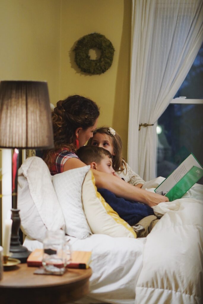 mom reading a book to two kids in bed