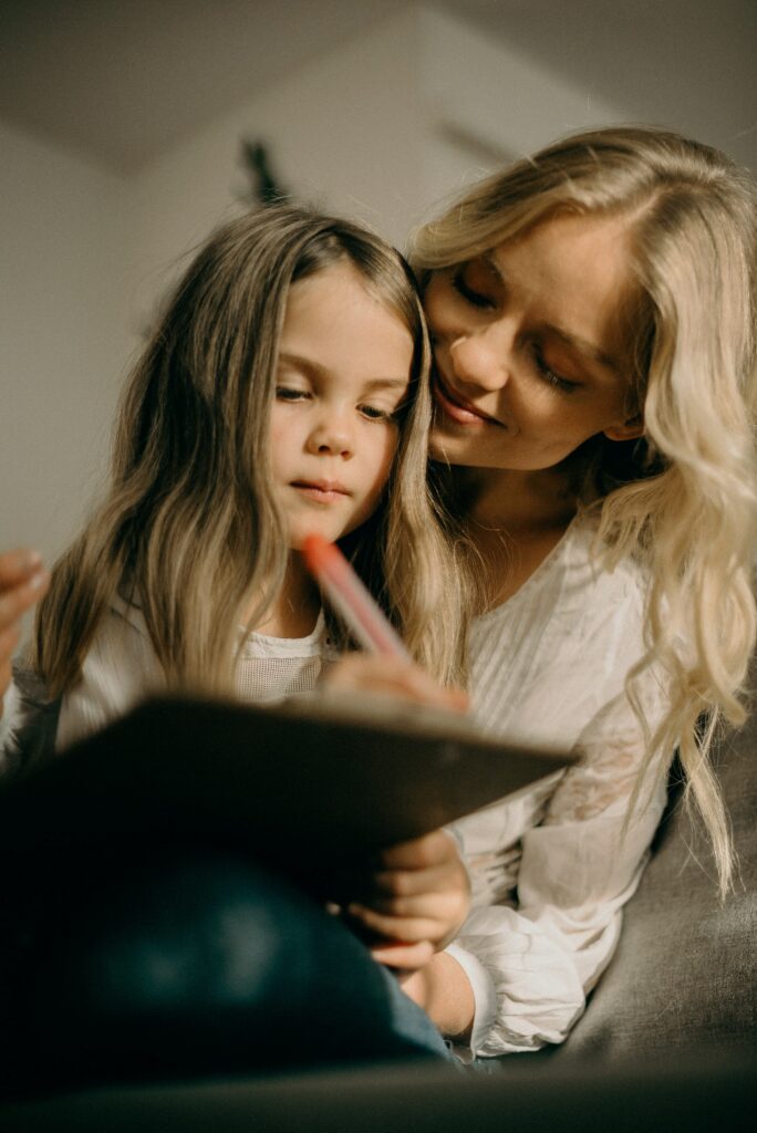 Little girl writing on clipboard with mom next to her as a New Years Eve at Home idea to write a family bucket list