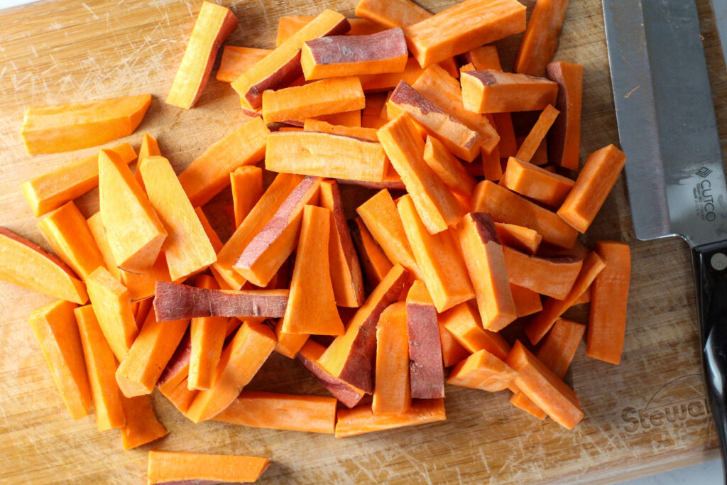 cutting board covered in raw sweet potato fries