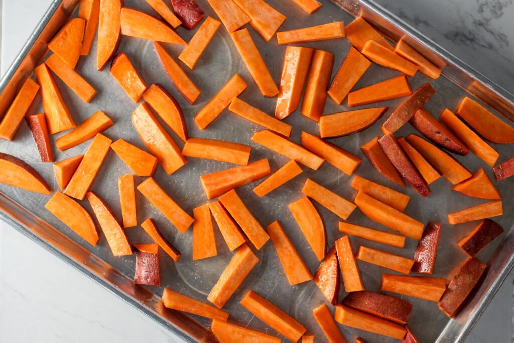 baking tray filled with a single layer of raw sweet potato fries