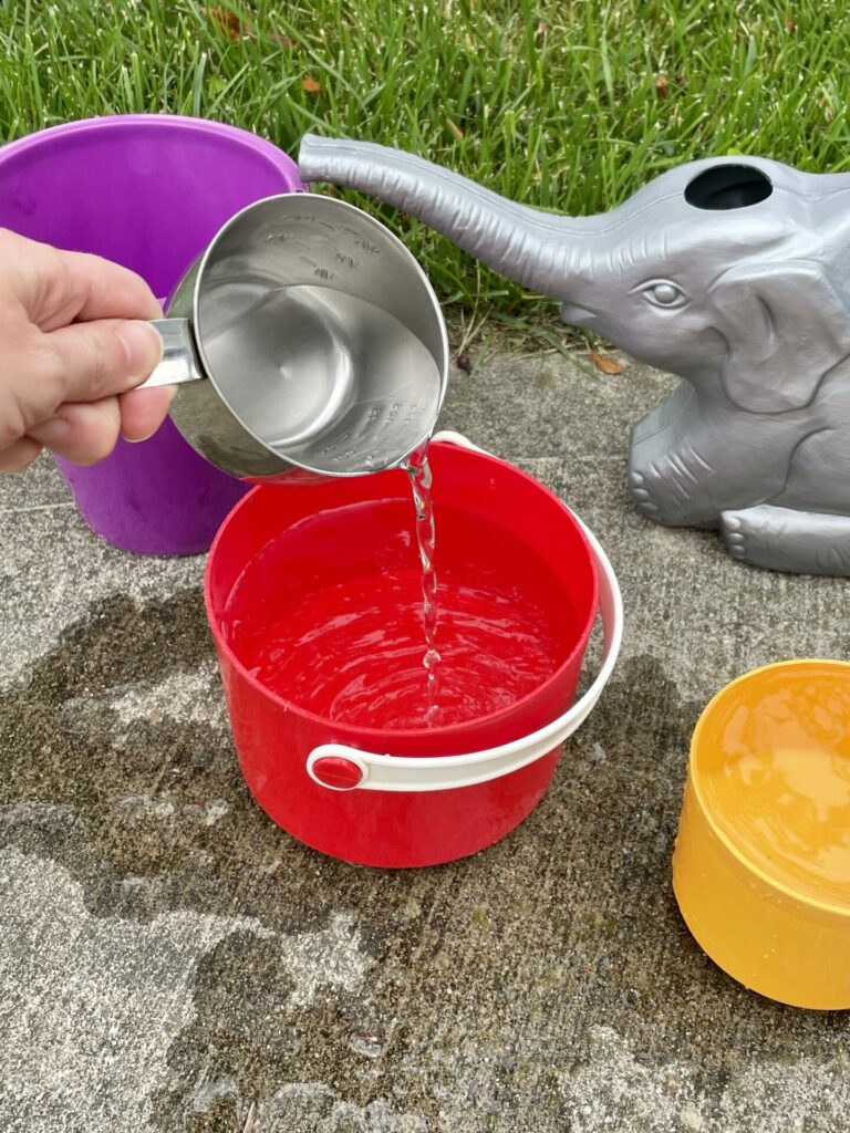 hand pouring water into red bucket for easy backyard summer activities