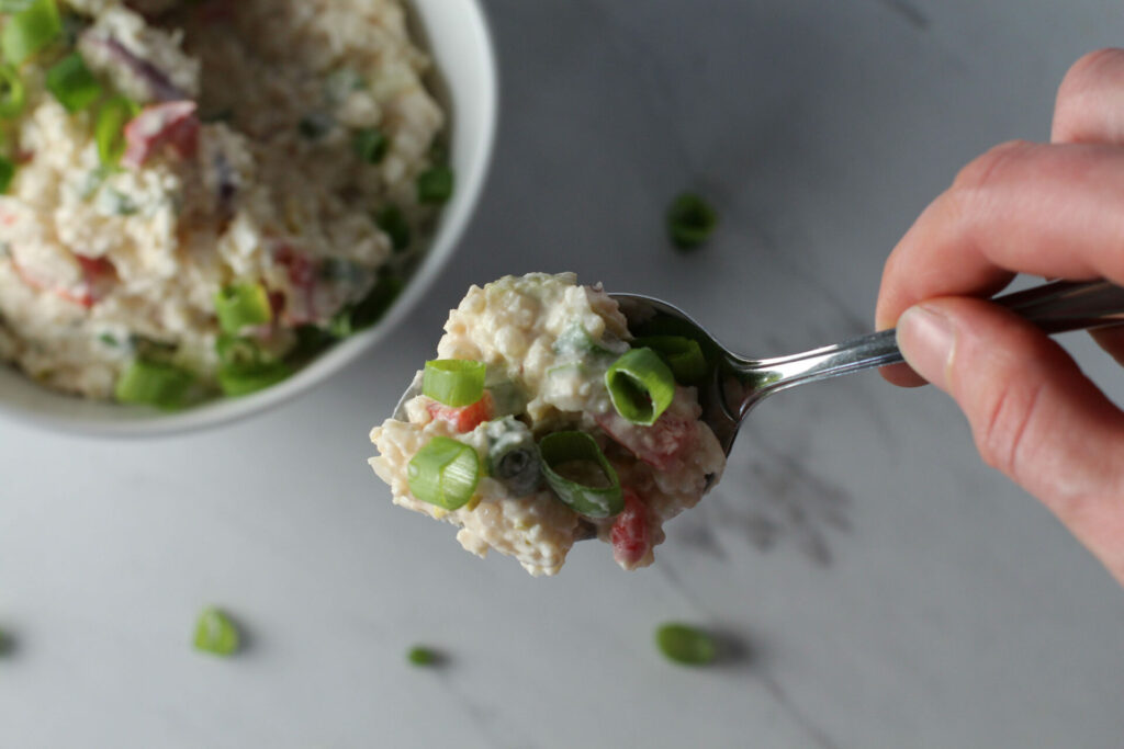 hand holding spoon with a bite of bacon cauliflower "potato" salad
