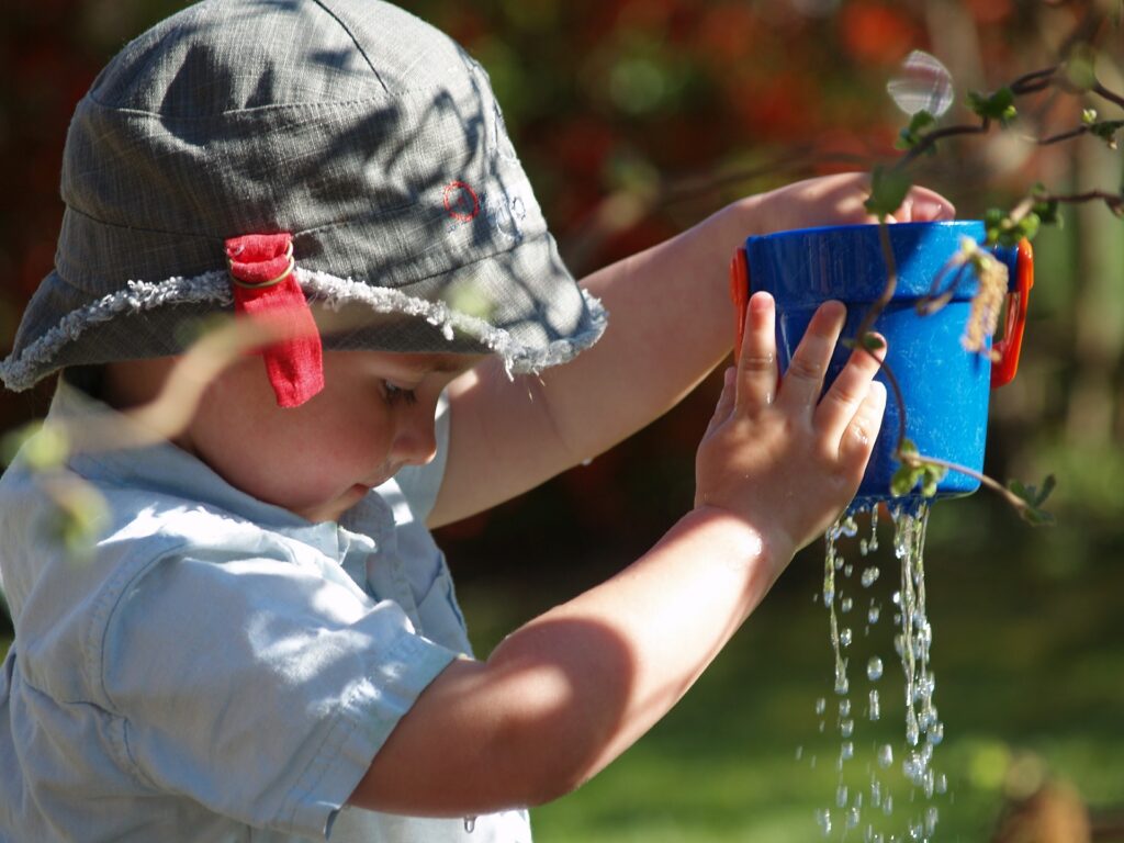 little boy holding up toy with water dripping out of the bottom