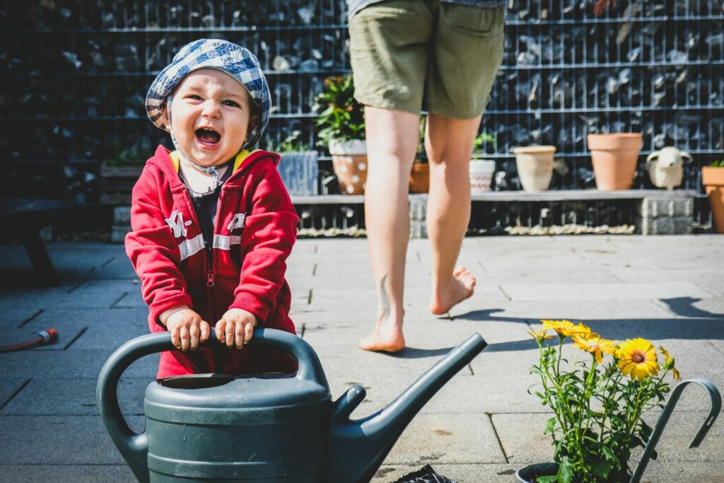 little boy with water pitcher in hand standing next to yellow flowers