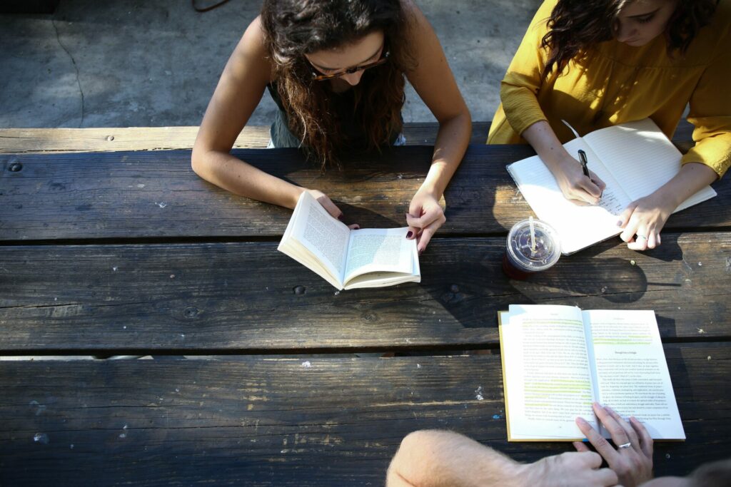 three people sitting at wooden table reading books and taking notes