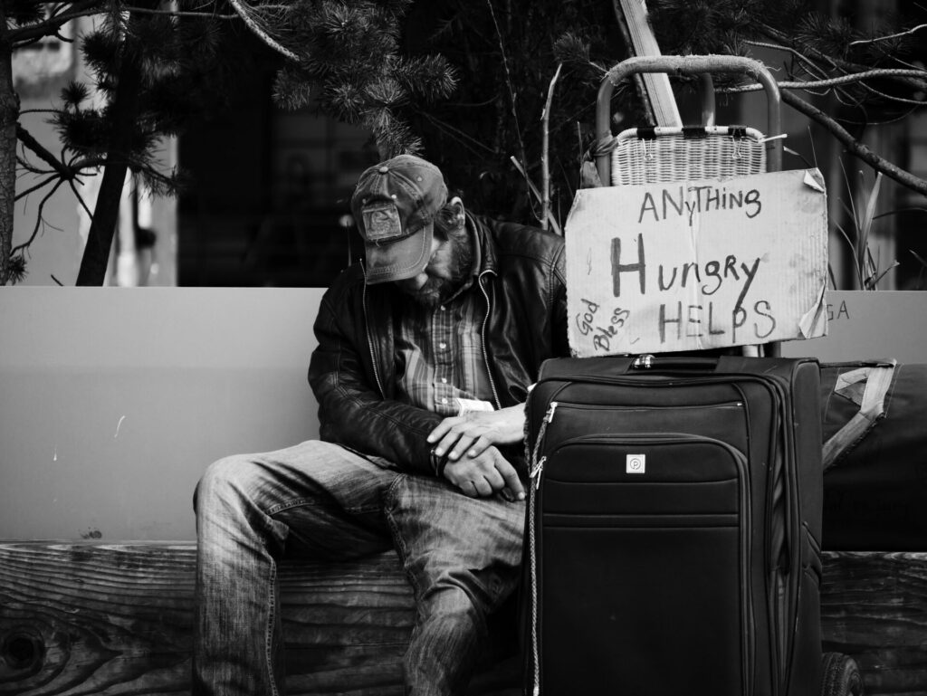 homeless man with a sign on a quitcase that says hungry anything helps