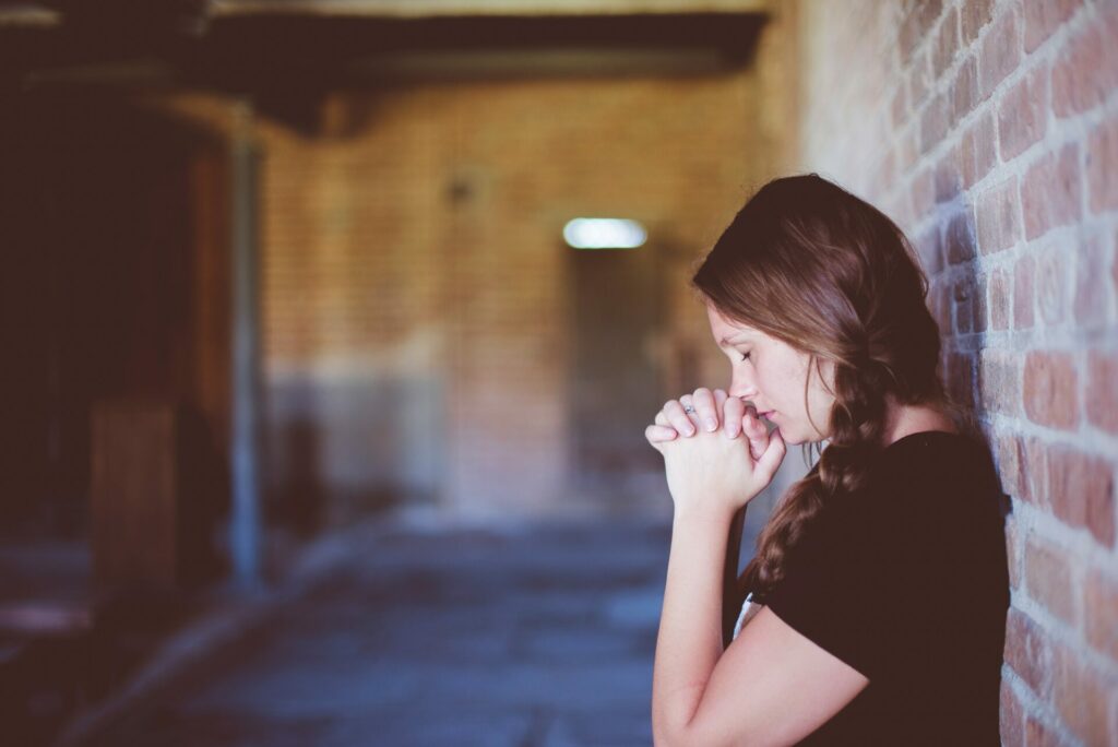 woman with back against brick wall praying