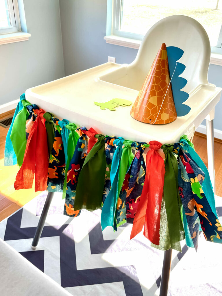 high chair decorated with dinosaur fabric banner and dinosaur party hat