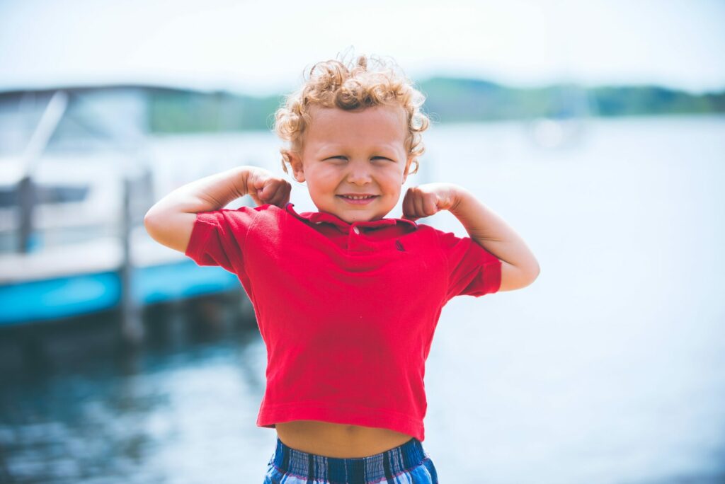 boy flexing his muscles outside to show that a benefit of outdoor play is increased strength