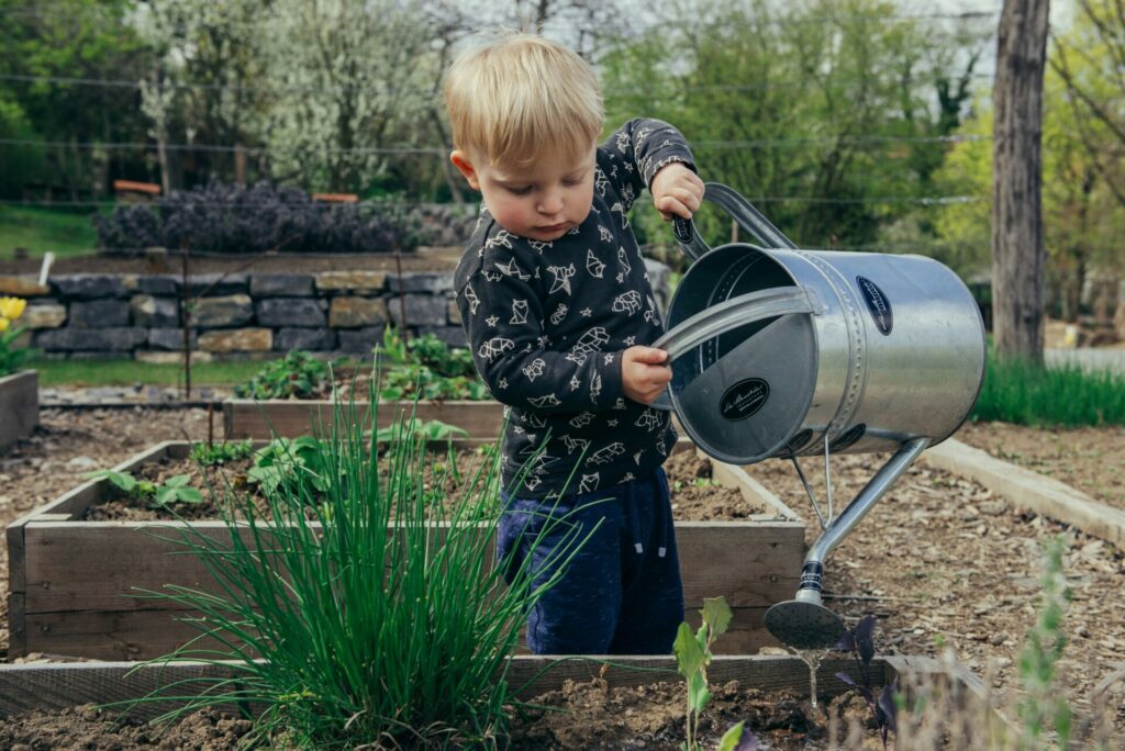 child watering garden as a benefit of outdoor play is learning about responsibility