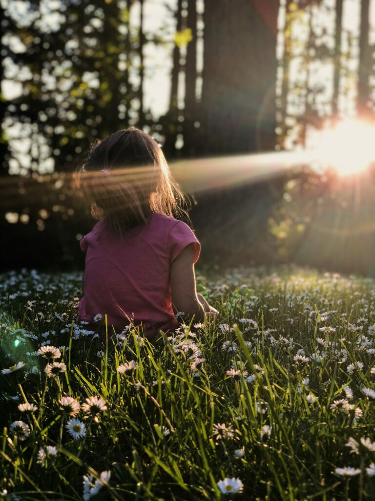 child sitting in field with sunlight shining on her