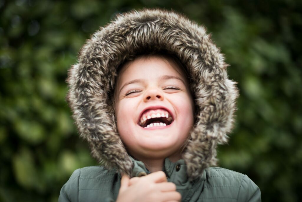 child with big smiling standing outside since a benefit of outdoor play is a better mood